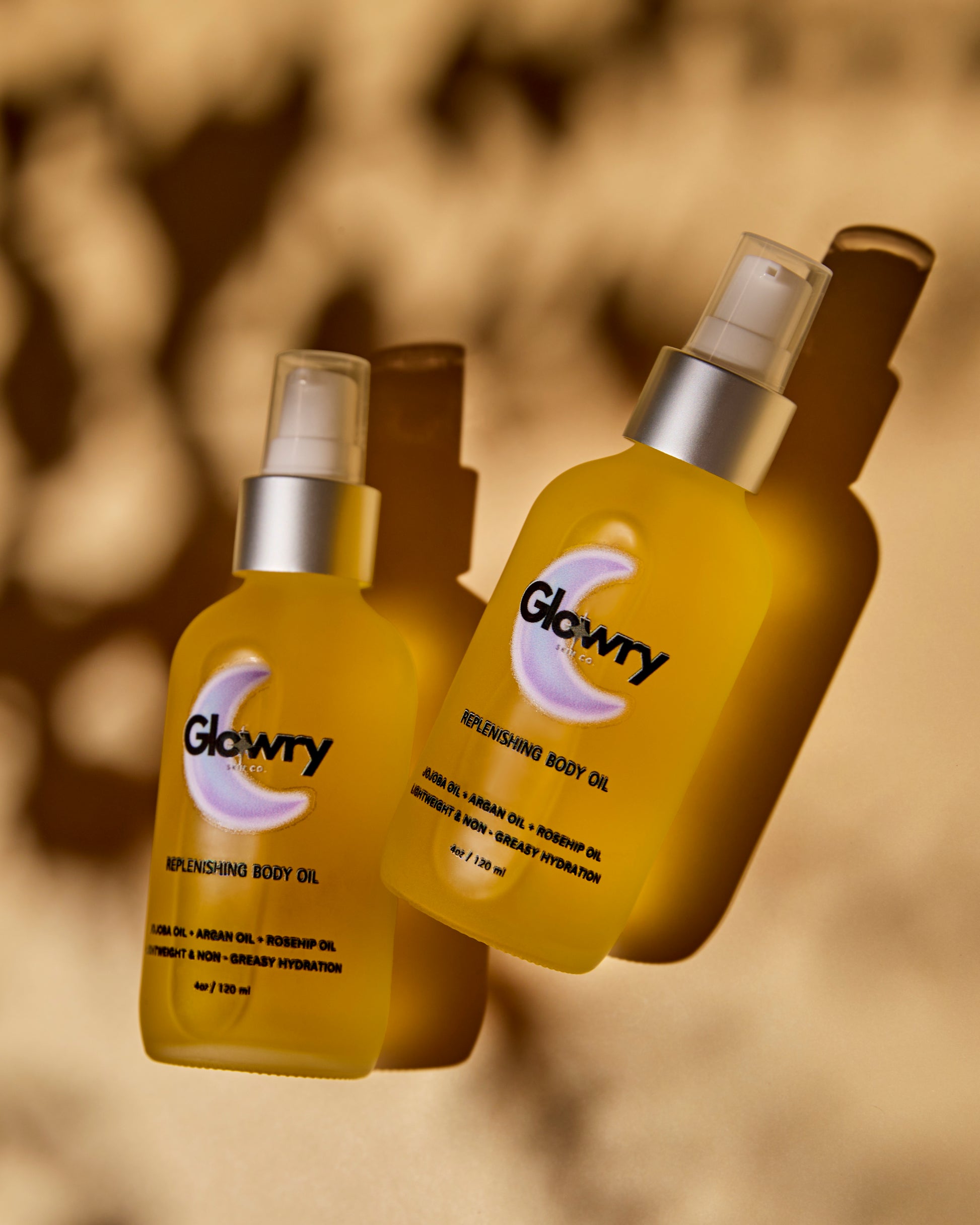 Aesthetic product shot of two Glowry Skin Co. Replenishing Body Oil bottles on a neutral beige background.